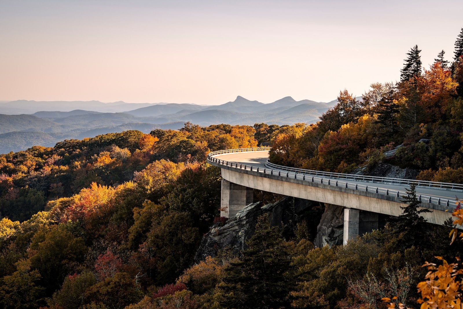 Your Guide to the Blue Ridge Parkway Near Asheville 1 A viaduct bridge hugging a mountain of fall colors with blue mountains in the distance on the Blue Ridge Parkway.