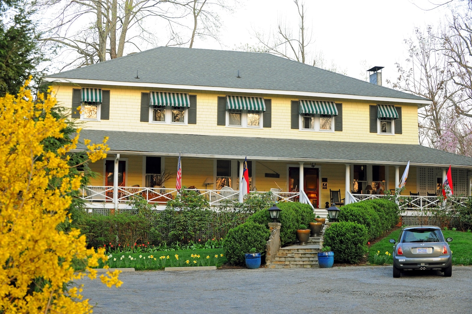 The front of a Saluda Bed and Breakfast, The Orchard Inn, with a yellow exterior framed by fall leaves.