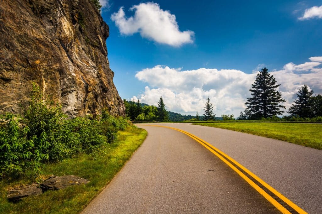 Visit These North Carolina Mountain Towns 1 Driving the Blue Ridge Parkway is one way to visit North Carolina mountain towns. Here the road bends to the left around a mountain face.